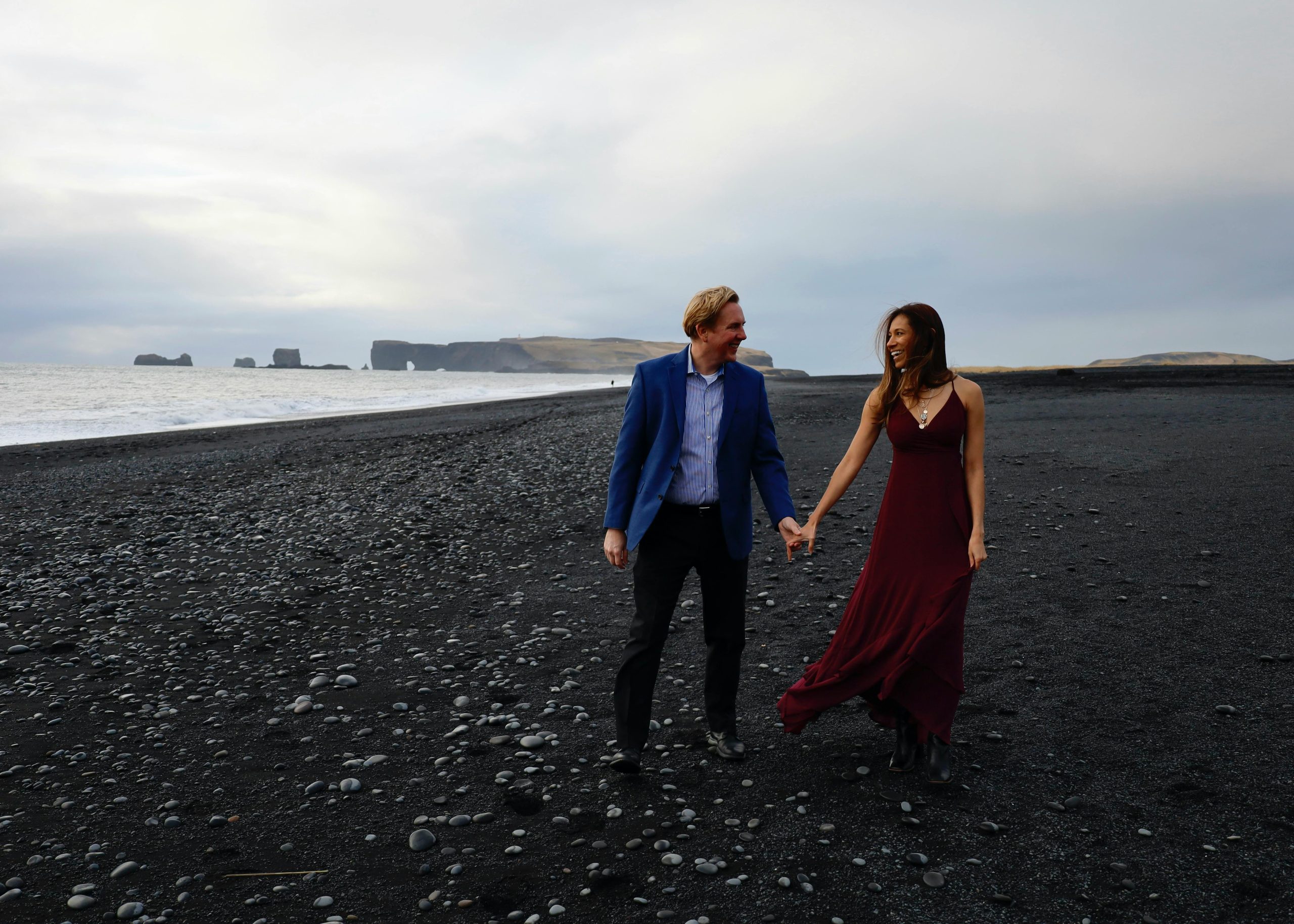 Couple walking hand in hand on the black sand beach of Vík í Mýrdal, creating a romantic moment.